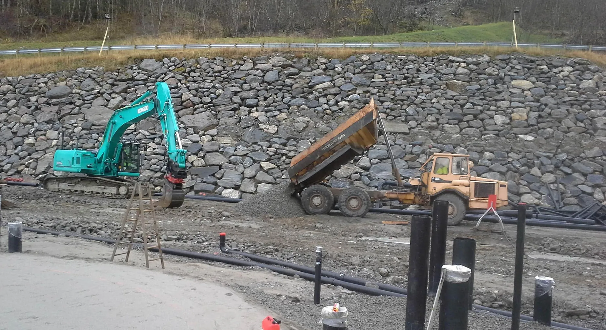 Gravemaskin og dumper frå A og J Bjordal ved ein nymura steinvoll